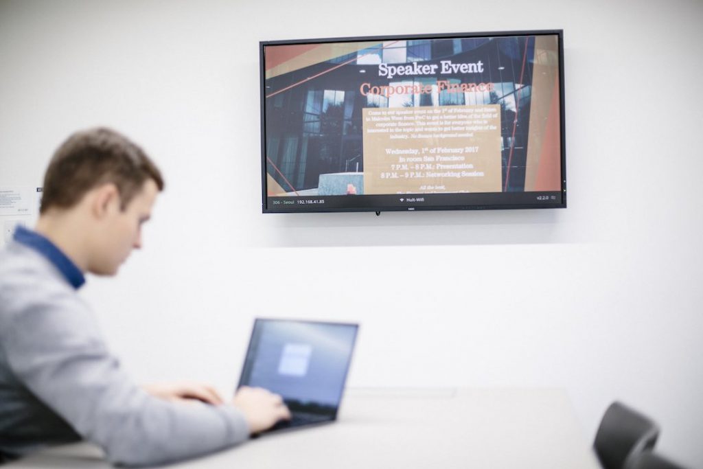 A student using a laptop connected to Airtame and a screen showing a customized background