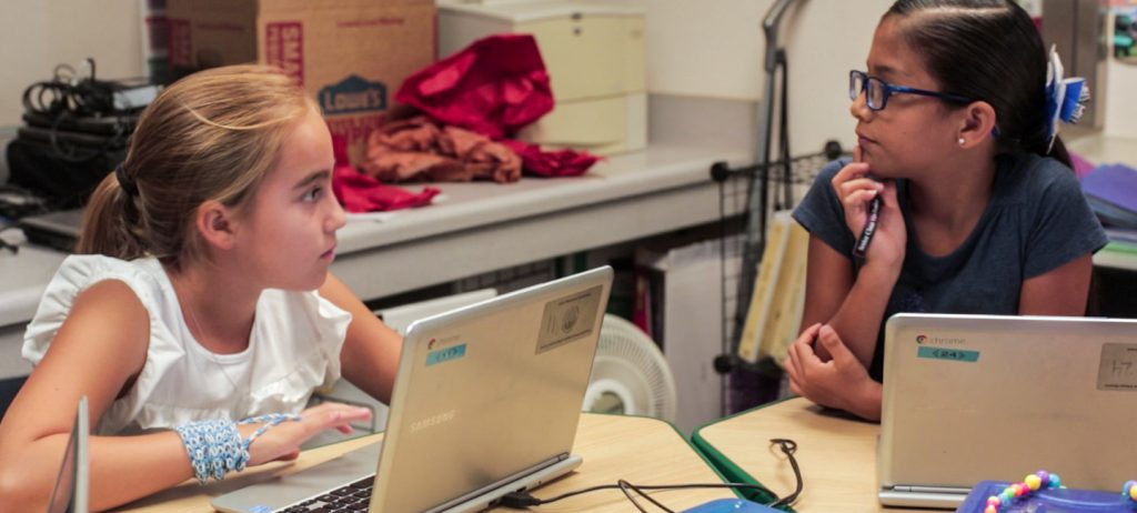 Two girls in a classroom using computer connected to Airtame