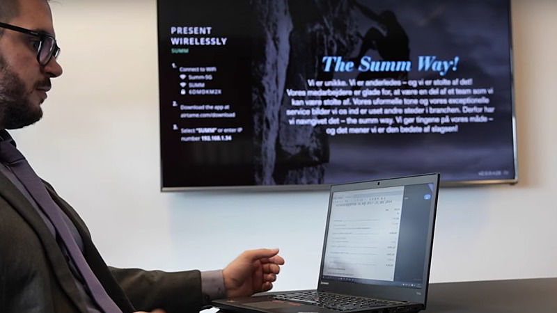 Man looking at his laptop while presenting wirelessly to a screen behind him