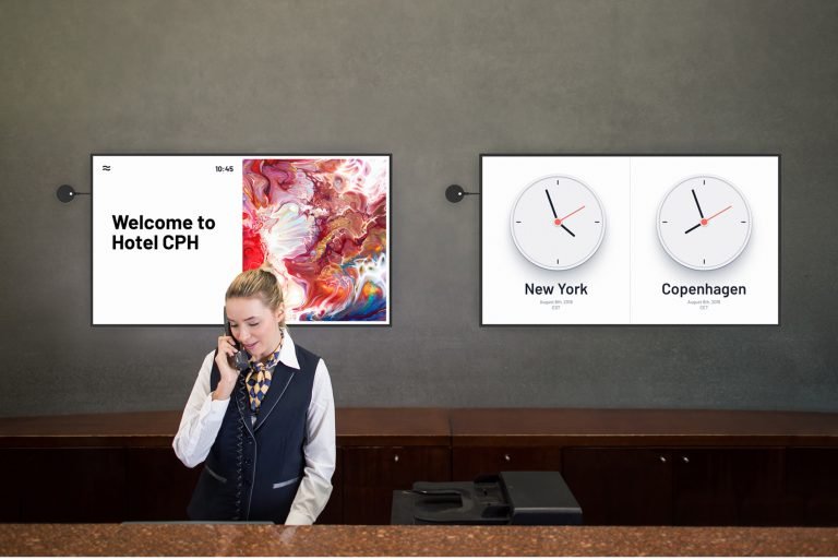 hotel lobby with two signs displaying a welcome message and a world clock behind woman who is on the phone